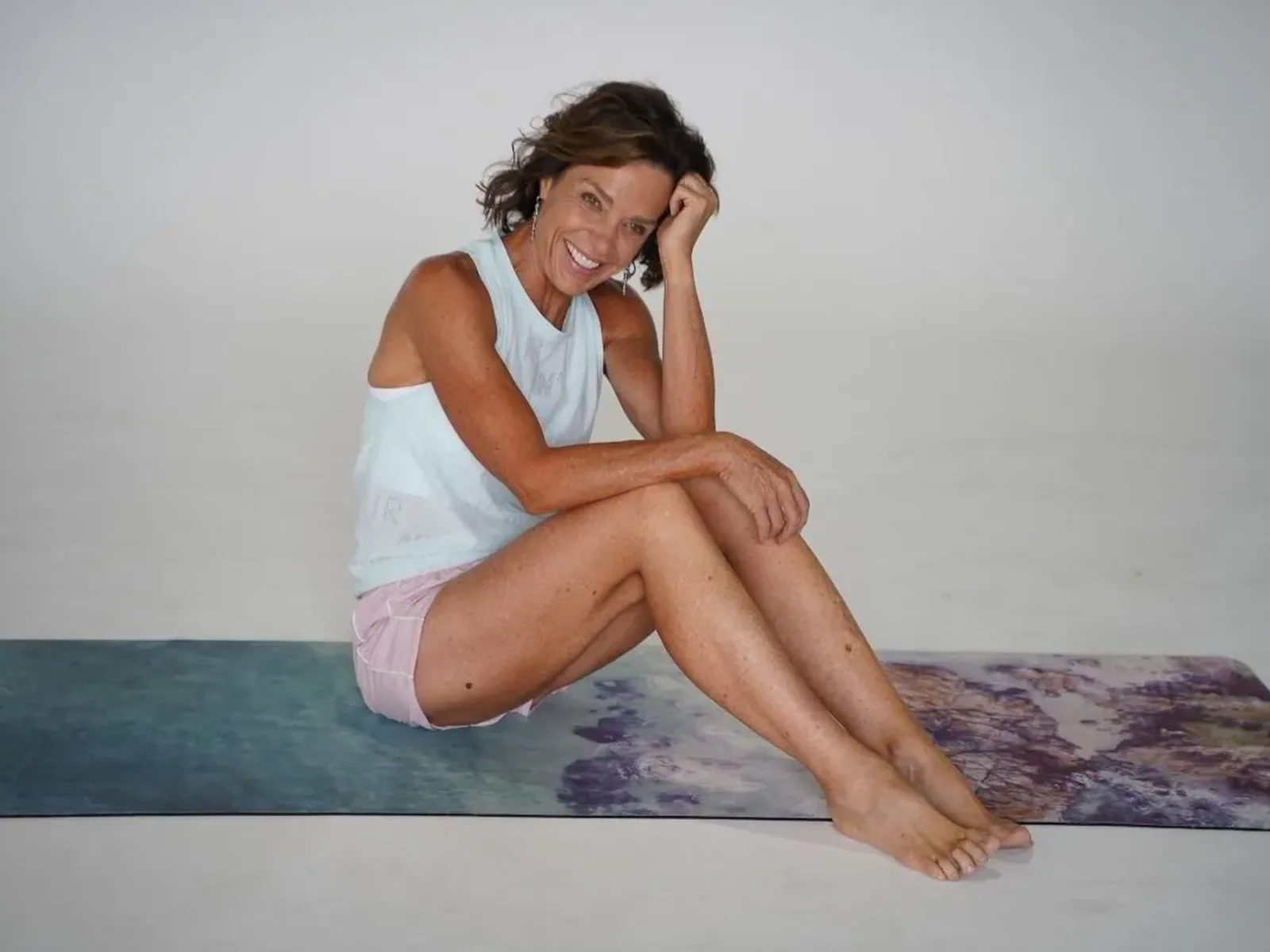 A woman in her fifties following a live class on a laptop at home, dumbbell in hand