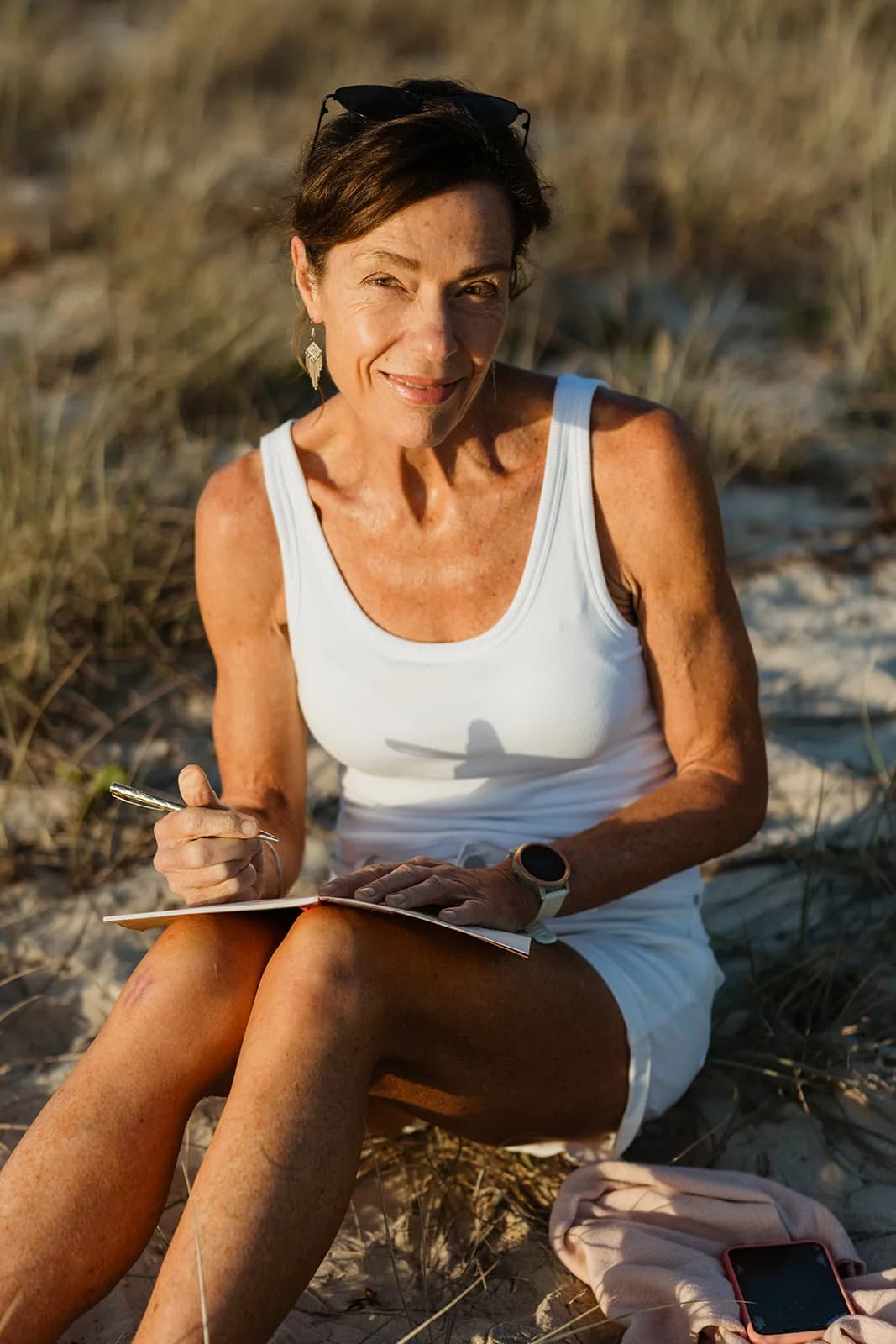 Dana Eden journaling in the dunes, smiling at the camera