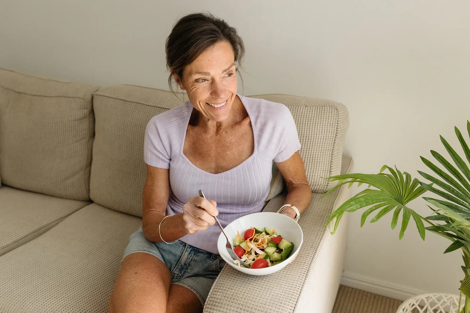 Dana Eden eating a bowl of salad on the couch