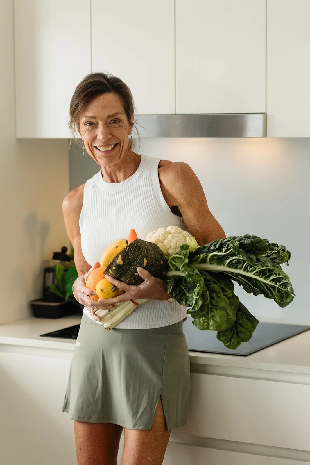 Dana Eden in her kitchen with an armful of vegetables, smiling