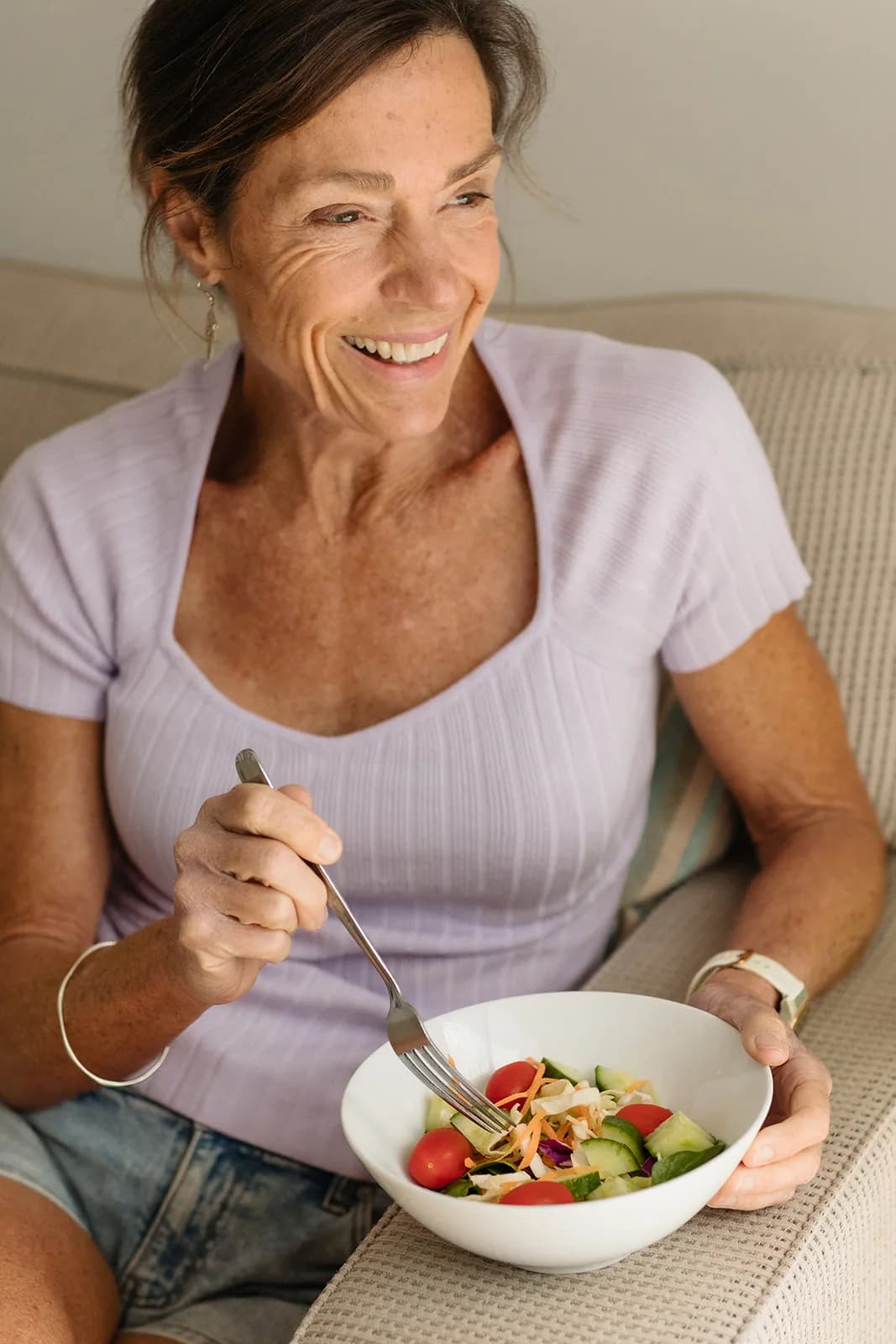 Dana Eden eating a bowl of salad on the couch